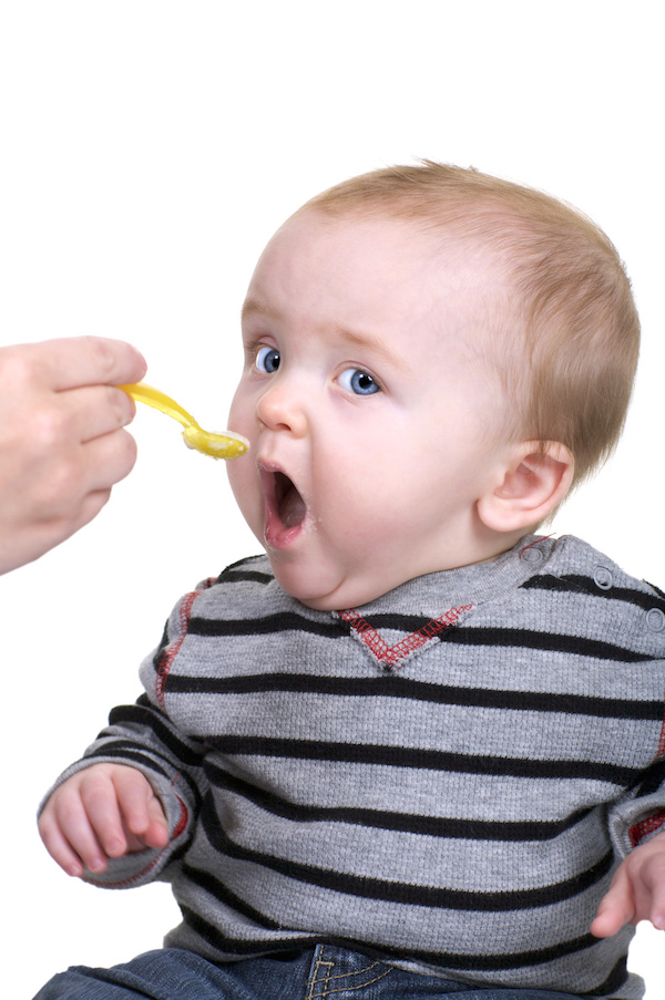 Cute baby being feed rice cereal with a yellow spoon, vertical